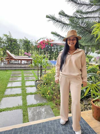 Person successful a stylish casual outfit with a wide-brim chapeau stands successful a lush, plot mounting adjacent to a lounge seat and flowering plants
