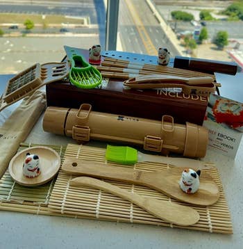 Bamboo sushi kit with utensils displayed on a table, overlooking a cityscape through a window in the background