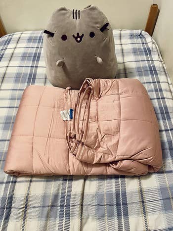 reviewer photo of pink folded weighted blanket next to Pusheen plushie