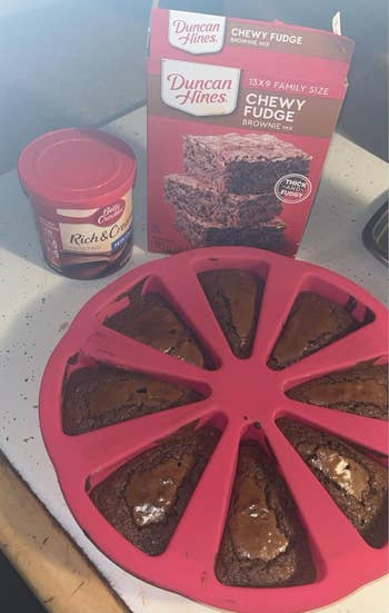 A photo of freshly baked brownies in a slice-shaped silicone pan next to Duncan Hines brownie mix and Rich & Creamy frosting