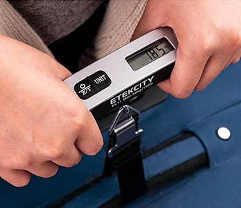 hands using the silver luggage scale to weigh a suitcase