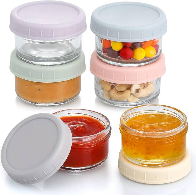 Four stackable glass jars with various contents like spreads and snacks, featuring pastel-colored lids
