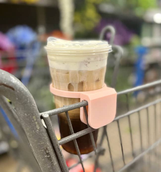A clip-on pink 3D-printed drink holder attached to the side of a grocery cart 