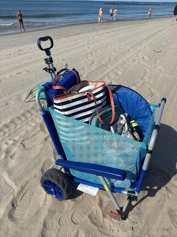 Beach cart filled with bags and items, with people and the ocean in the background