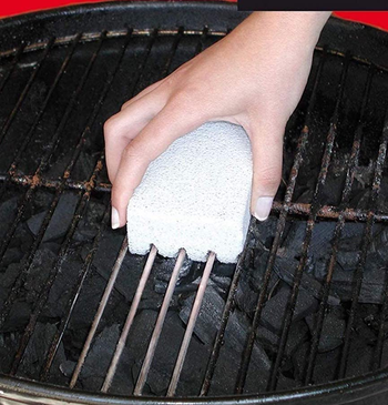 photo of someone using the stone to clean a grill grate, showing how the area that the stone has been used on looks much cleaner than the rest