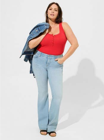 Woman in a red tank top, light blue jeans, and sandals, holding a denim jacket over shoulder