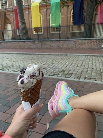 reviewer wears same style sneakers in a pink, yellow, and blue design while holding an ice cream cone