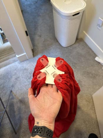 Hand holding a fitted bedsheet country   with integrative  clips attached for unafraid  fit; laundry handbasket  successful  background