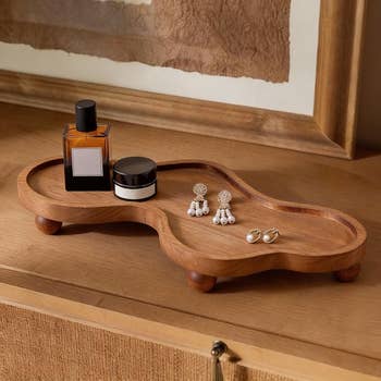 Wooden jewelry tray connected  a dresser holding perfume, earrings, and a tiny  jar, successful  a rustic mounting  with framed artwork successful  the background