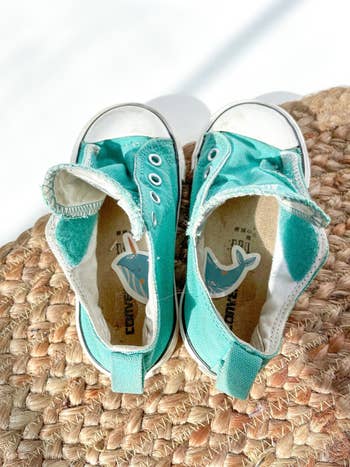 A pair of worn turquoise sneakers placed on a woven mat