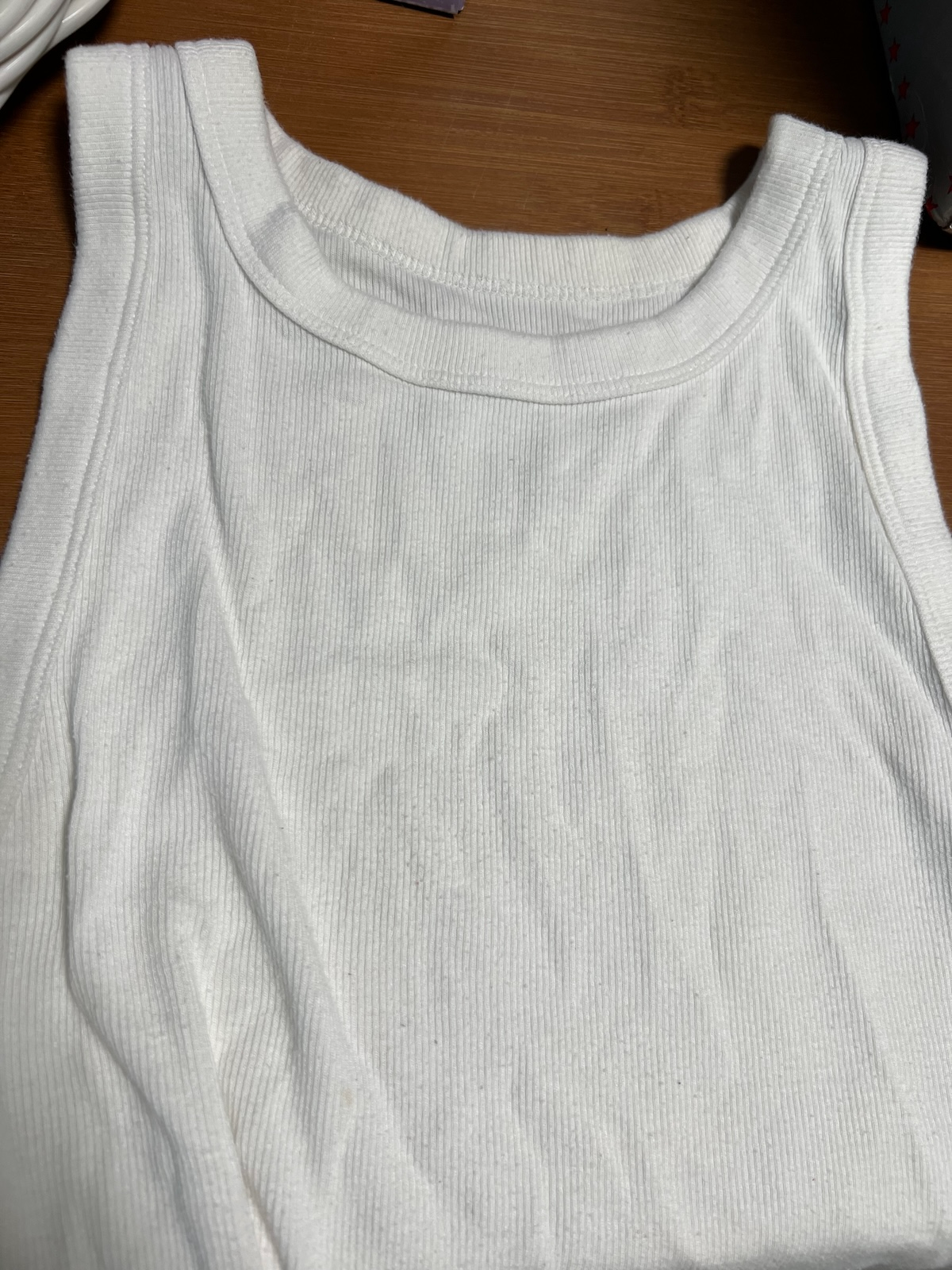 White ribbed tank top on a wooden surface, showcasing its simple texture and neckline. Perfect for casual styling or layering