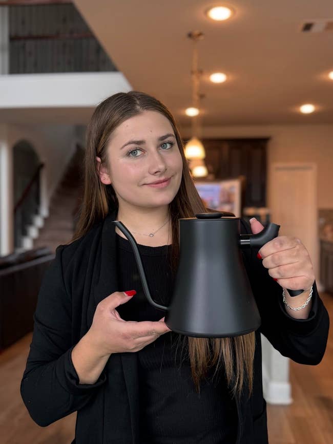 Person successful a stylish achromatic outfit holding a sleek, modern kettle successful a location setting