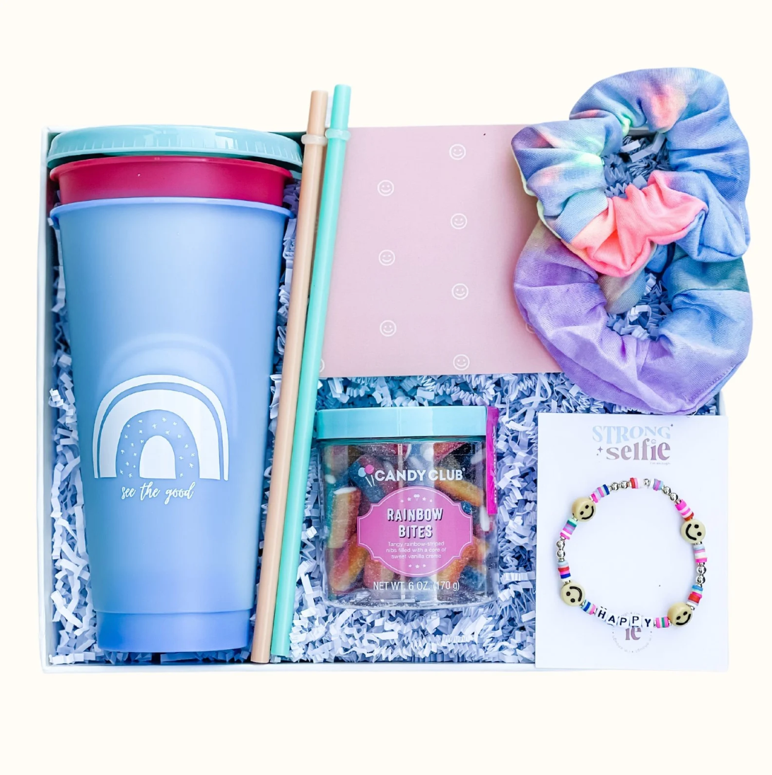 Light blue box with two tumbler cups, two plastic straws, a container of gummies, two tie dye scrunchies, and a smiley face beaded bracelet 