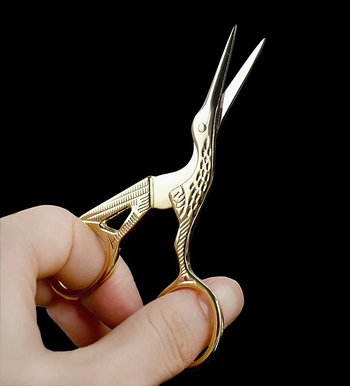 hand holding the gold crane-shaped scissors