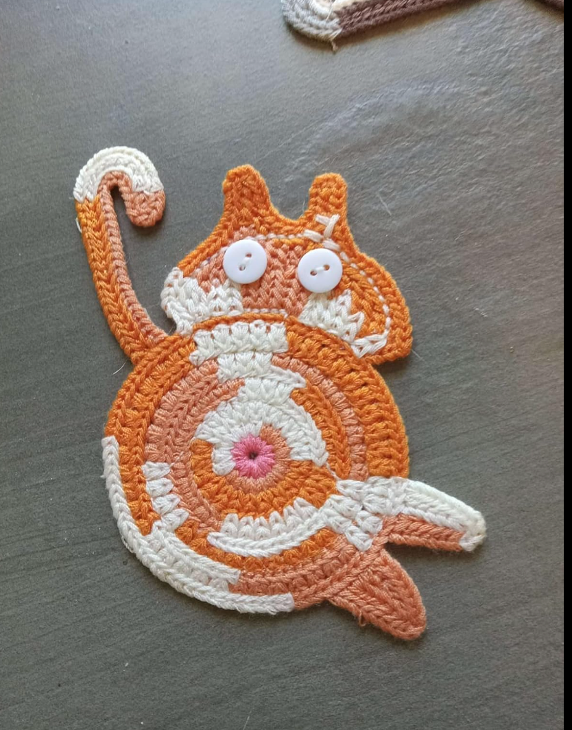 Crocheted cat-shaped coaster with spiral design and button eyes, suitable for home decor or gifts