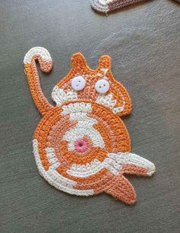 Crocheted cat-shaped coaster with spiral design and button eyes, suitable for home decor or gifts