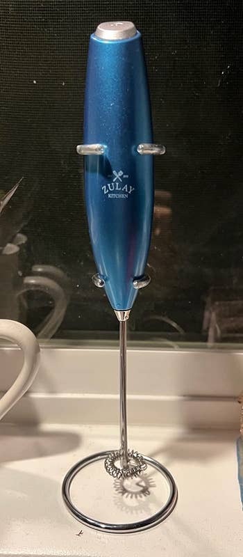 Reviewer image of blue handheld frother with silver button on top of handle on a counter
