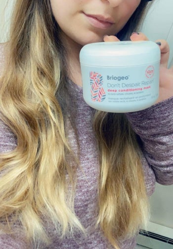 reviewer with wavy hair holding the jar of the product