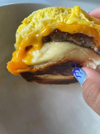 Hand holding a breakfast sandwich with melted cheese