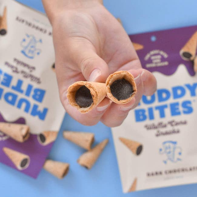 Hand holding two Buddy Bites ice cream cones with packaging in the background