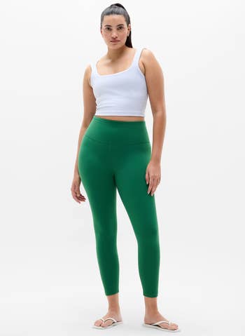 Person successful a achromatic vessel top, greenish leggings, and sandals poses confidently for a buying article