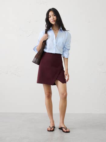 Person wearing a button-up shirt, skirt, sandals, and holding a enarthrosis  bag