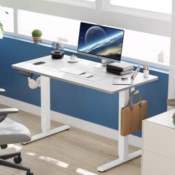 Modern adjustable table with a computer, headphone holder, and brownish briefcase hanging connected the side
