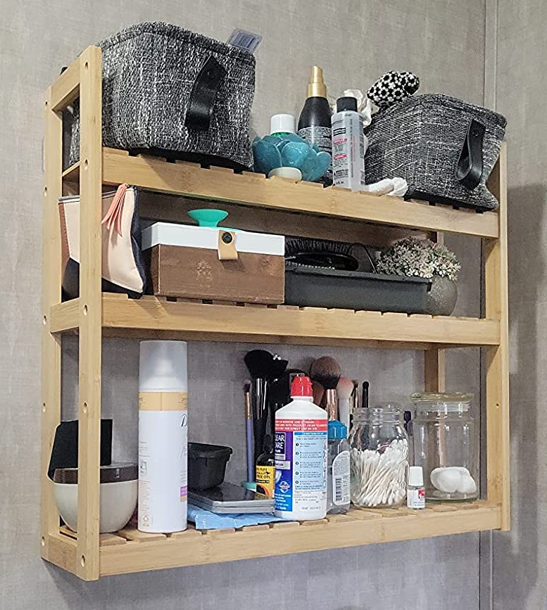 Reviewer image of a natural three-tier shelf mounted to wall with toiletries and bags