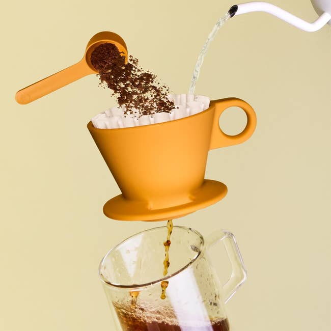 Coffee being brewed with a pour-over setup; a scoop of crushed coffee, blistery h2o pouring, and java dripping into a solid mug below