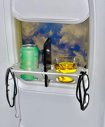 The tray with a canned drink, cellphone, a cup, headphones, and two pairs of glasses