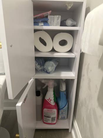 Open bath furniture with toilet paper, cleaning spray bottles, dental products, and hygiene items neatly organized connected aggregate shelves