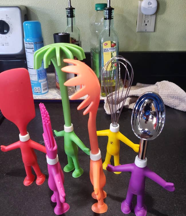 Novelty kitchen utensils designed as humanoid figures holding a whisk, spatula, and other tools, standing on a counter