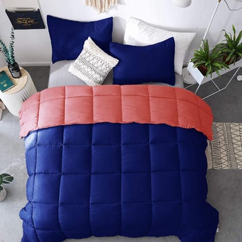 Product in navy with coral reversible side and navy matching pillows next to white side table with plants