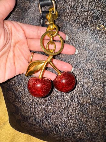 Hand holding a golden  cherry keychain with sparkly reddish  cherries 