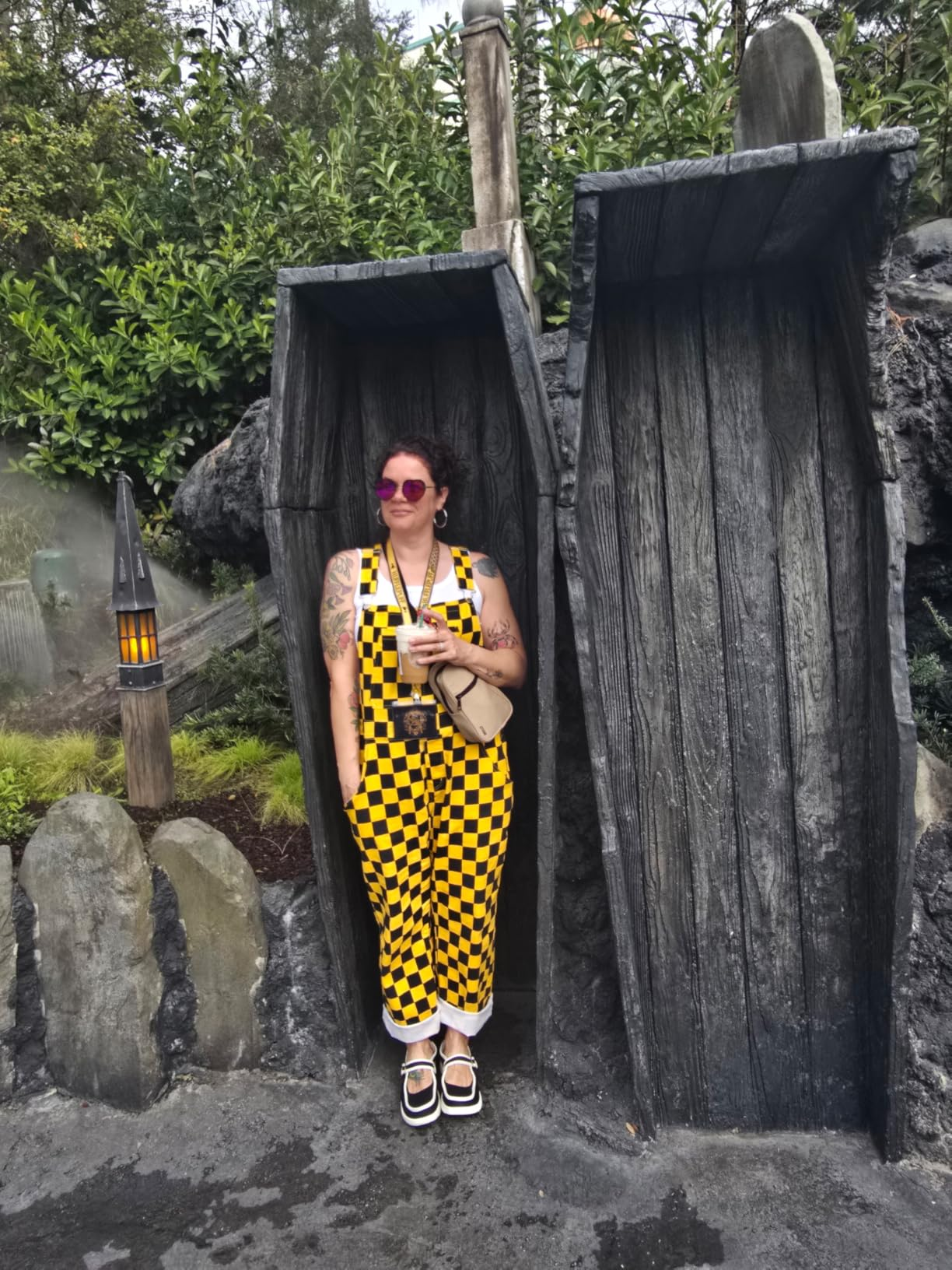 Person successful  achromatic  and yellowish  checkered jumpsuit with a camera astir   their neck, lasting  betwixt  2  woody  structures outdoors
