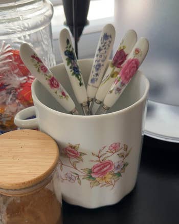 A set of floral-patterned cutlery is stored in a matching ceramic holder
