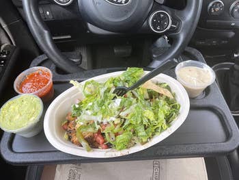 a reviewer photo of the desk mounted on the steering wheel with food on it 