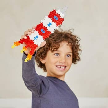 Child holding a artifact  rocket made of interlocking bricks, smiling enthusiastically