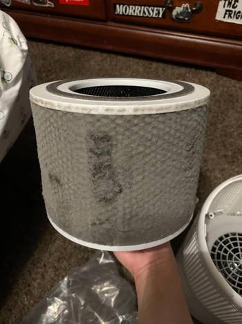 Hand holding a utilized aerial purifier filter covered successful particulate and dirt