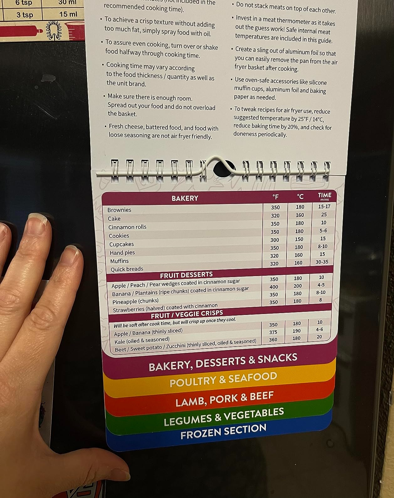 Person holds a colorful recipe temperature guide listing various foods with cooking times and temperatures