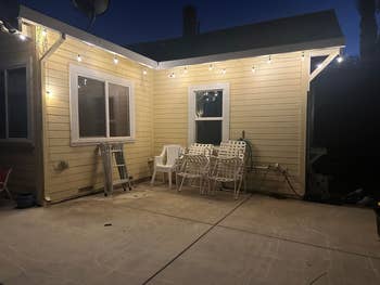 Patio with drawstring lights, aggregate stacked chairs, a ladder, and a hose by a location astatine dusk