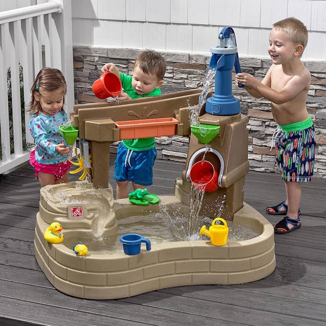 Three children play astatine a h2o enactment array with artifact buckets and ducks