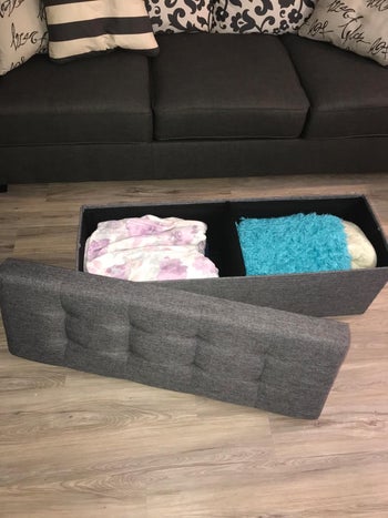 reviewer image of the open gray storage ottoman with blankets inside