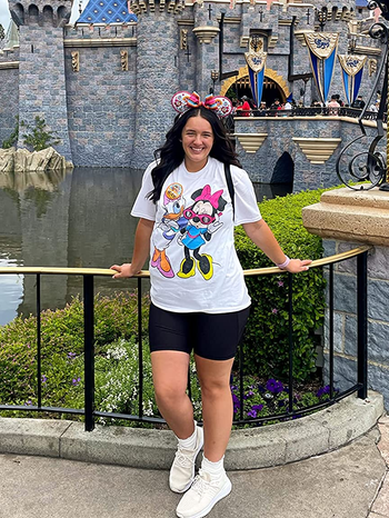 a reviewer at disney land wearing a white t-shirt with minnie mouse and daisy duck on it