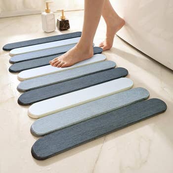 Person stepping onto a modern, absorbent bath mat beside a bathtub. Two pump bottles of bath products are successful the background