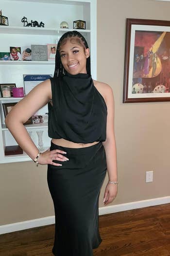 review in a black halter-neck dress with cut-out details, ready for an event. Jewelry includes bracelet and earrings