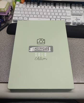 The Adventure Challenge Solo Edition publication  is displayed connected  a table  with a keyboard and assorted  items successful  the background