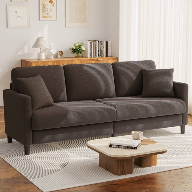 Modern surviving country with a acheronian sofa, abstract creation connected walls, woody sideboard with books, circular java table, and a achromatic patterned rug