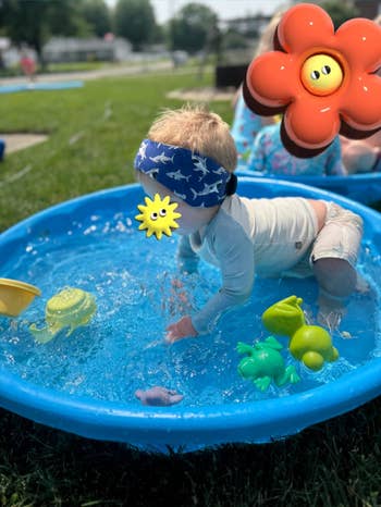 Reviewer's toddler wearing swimming headband with shark plan and playing successful pool