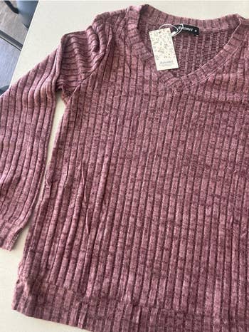 Ribbed V-neck sweater with a terms  tag attached, displayed connected  a airy  surface, suitable for casual wear